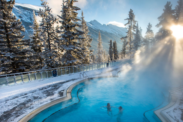 Banff Upper Hot Springs pool on a clear day with a view Mount Rundle in the distance framed by snow frosted trees