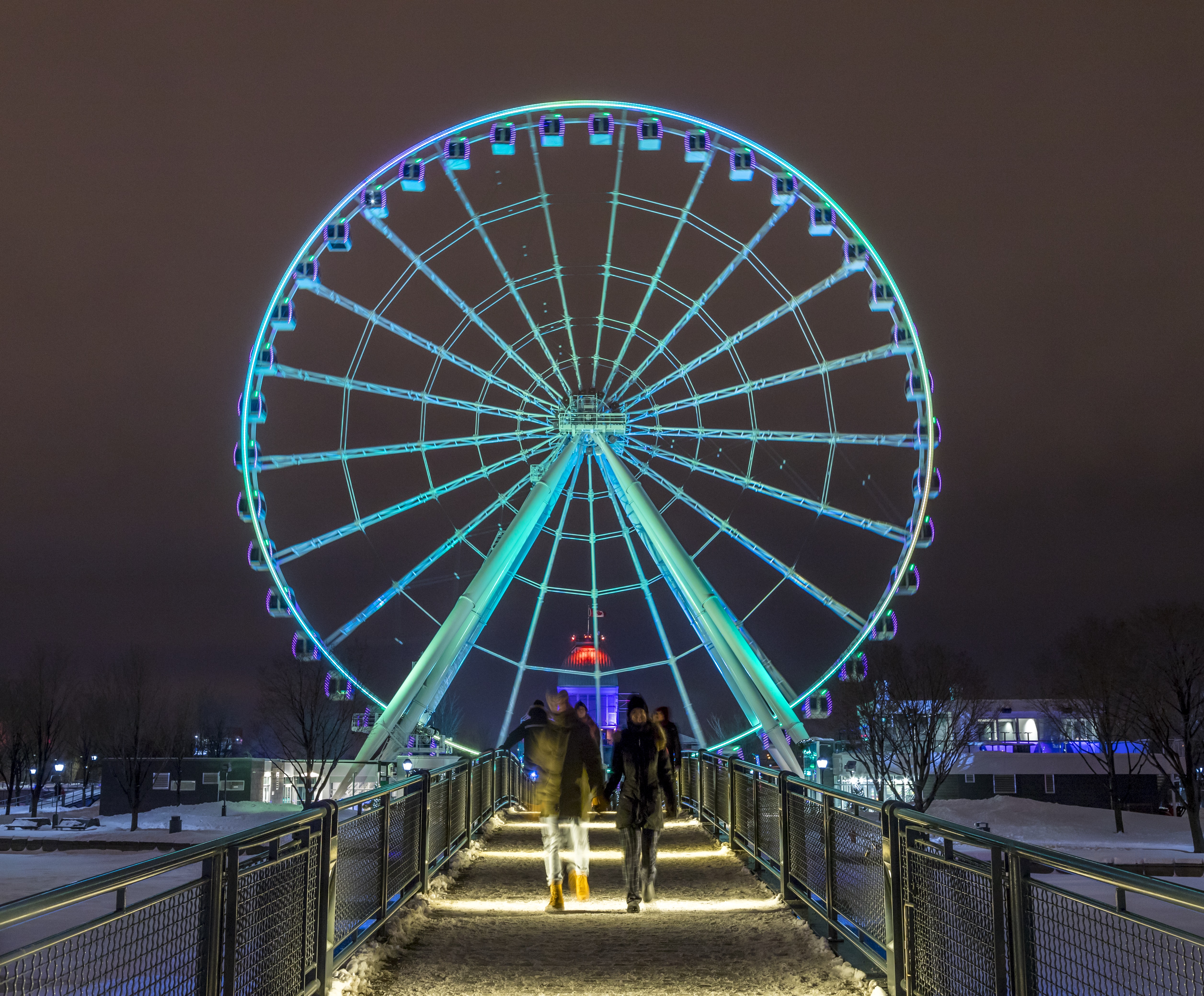 People walking in front of a large ferris wheel lit up at night in winter