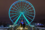 People walking in front of a large ferris wheel lit up at night in winter