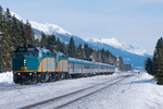 Incoming VIA Rail train journeys through scenic passage of trees and snowcapped mountains