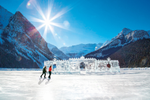 A couple skates in front of an ice castle on frozen Lake Louise with snowy mountains behind