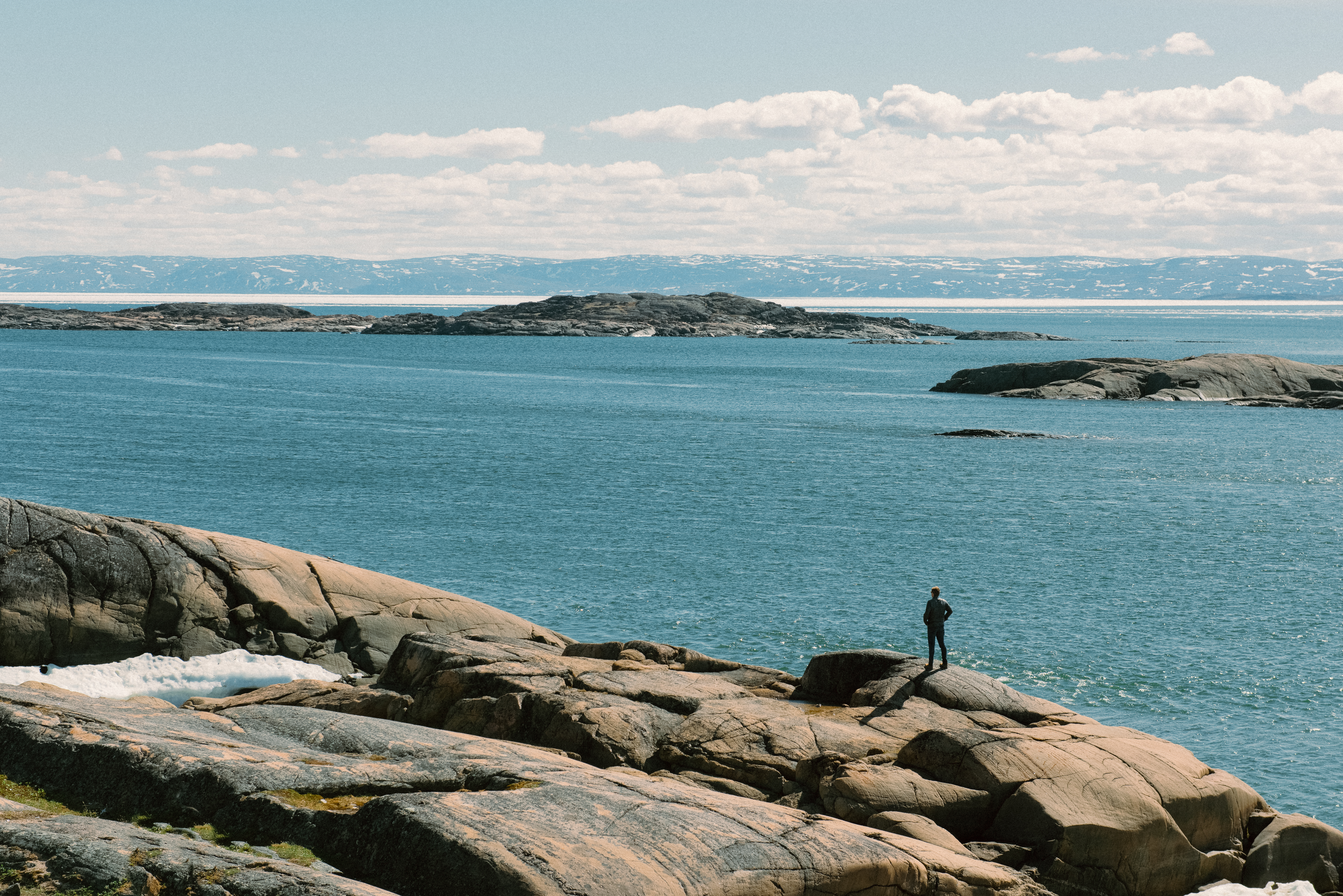 A man stands on large rocks looking out at the sea