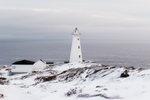 View of lighthouse on snowy cliff with a view of the sea in the distance