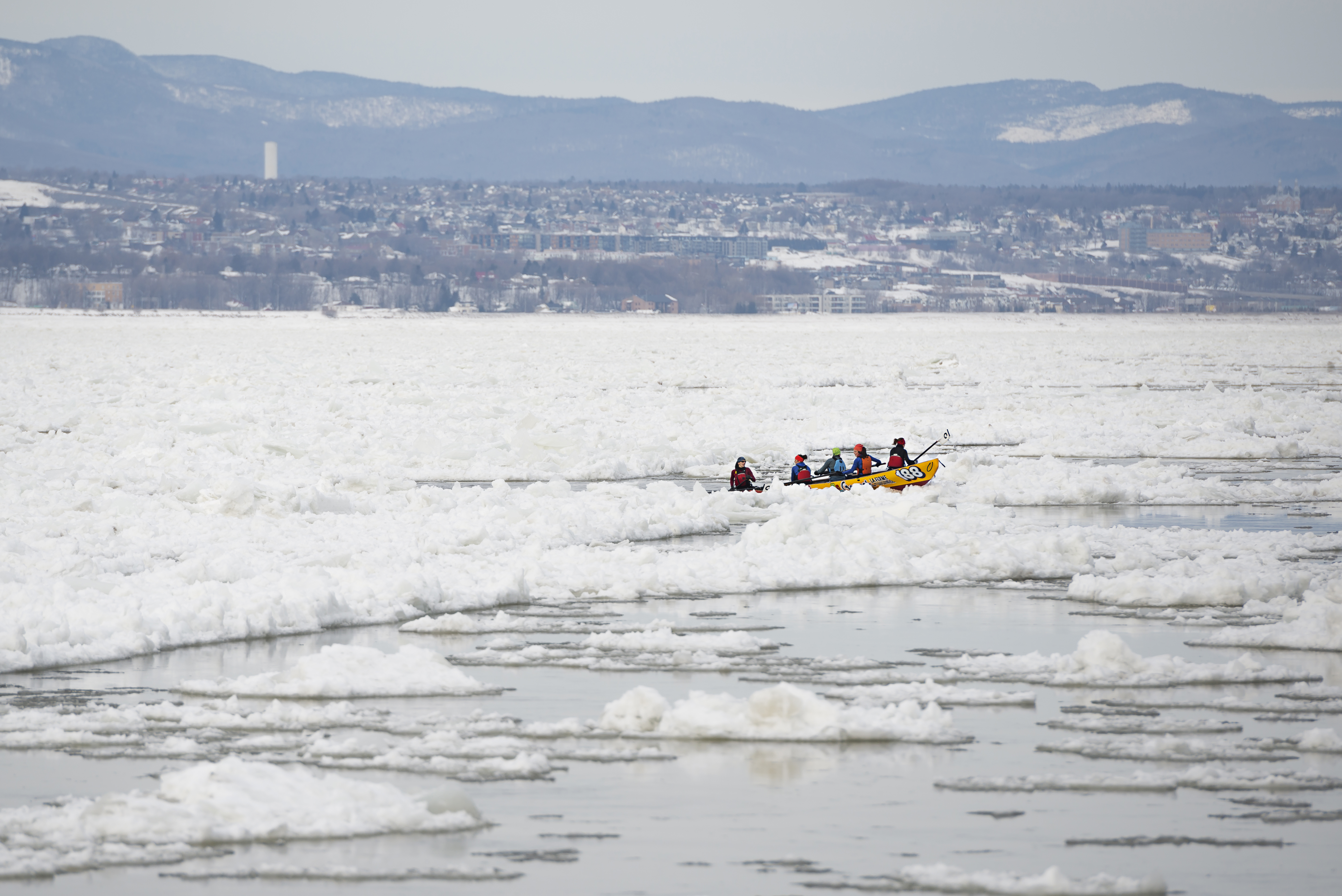 A canoe team racing through the ice on the river during the Quebec Winter Carnival