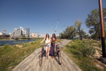 Two friends walking their bikes along the riverwalk during summer on St. Patrick’s Island