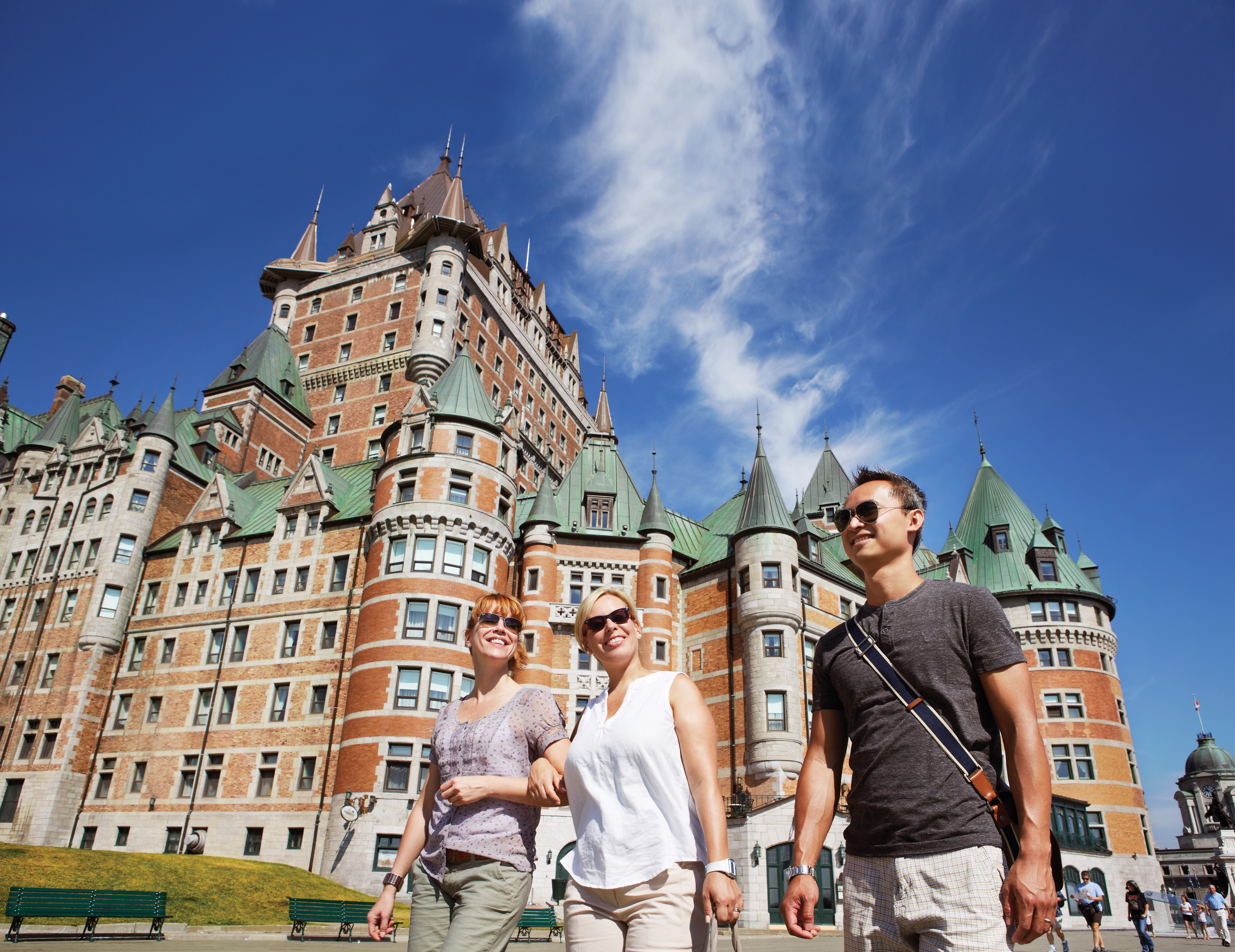 Three people walk past Le Chateau Frontenac hotel on a sunny day