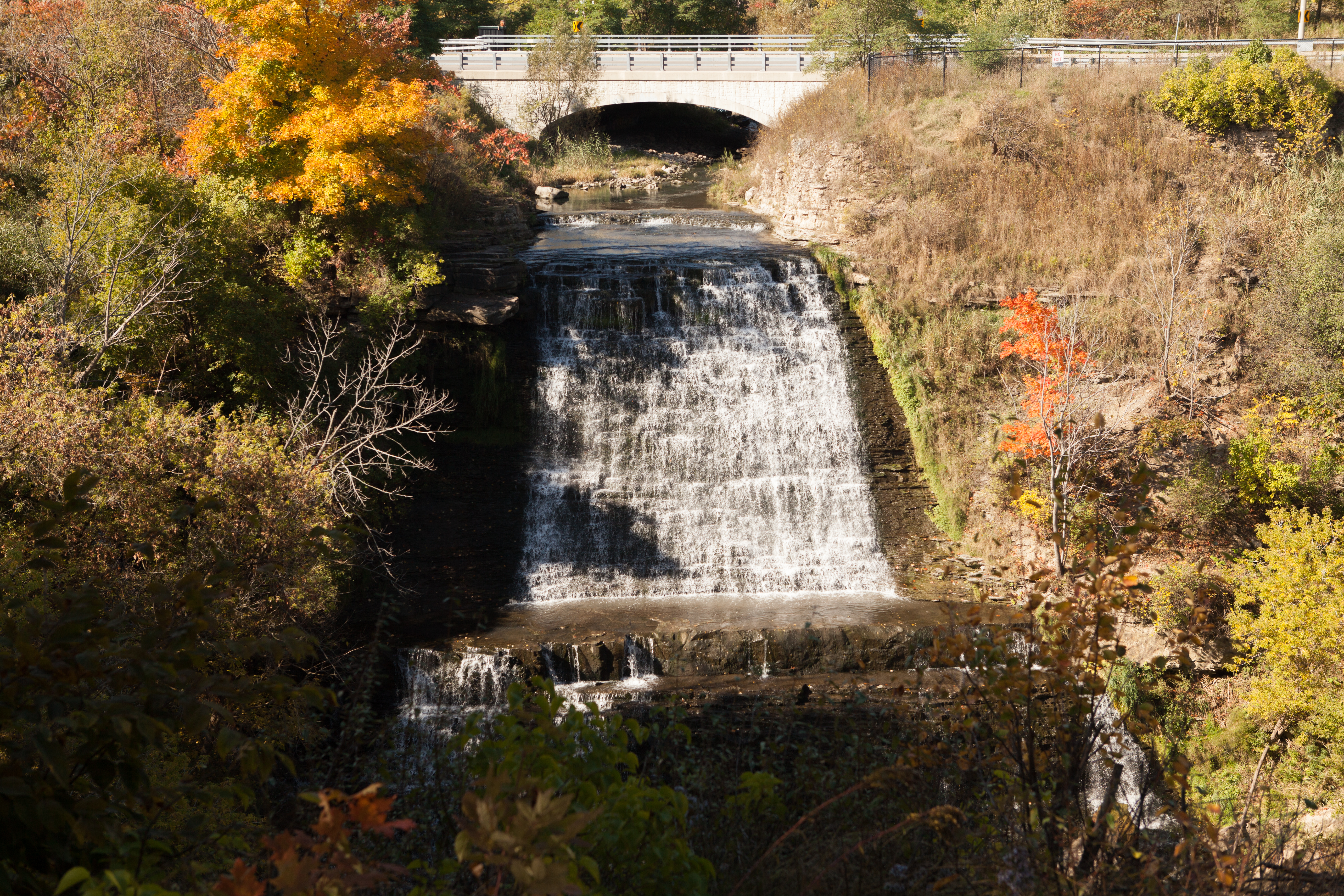 Water rushes down over steps formed by rock and waterfall framed by trees during fall