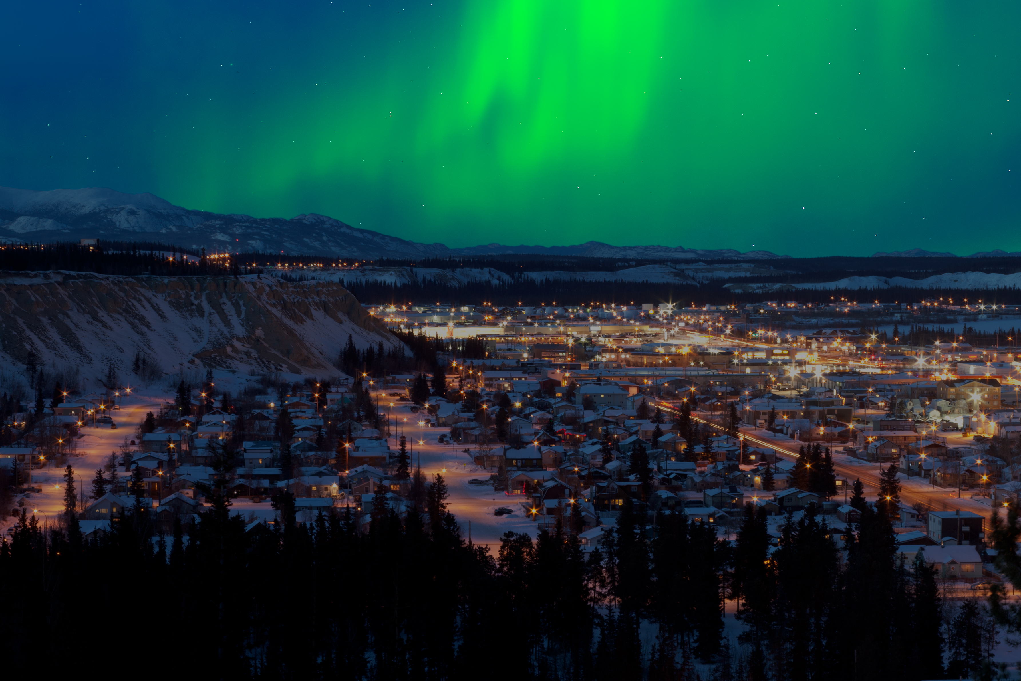Northern Lights turn blue sky green over snowy mountains and Downtown Whitehorse