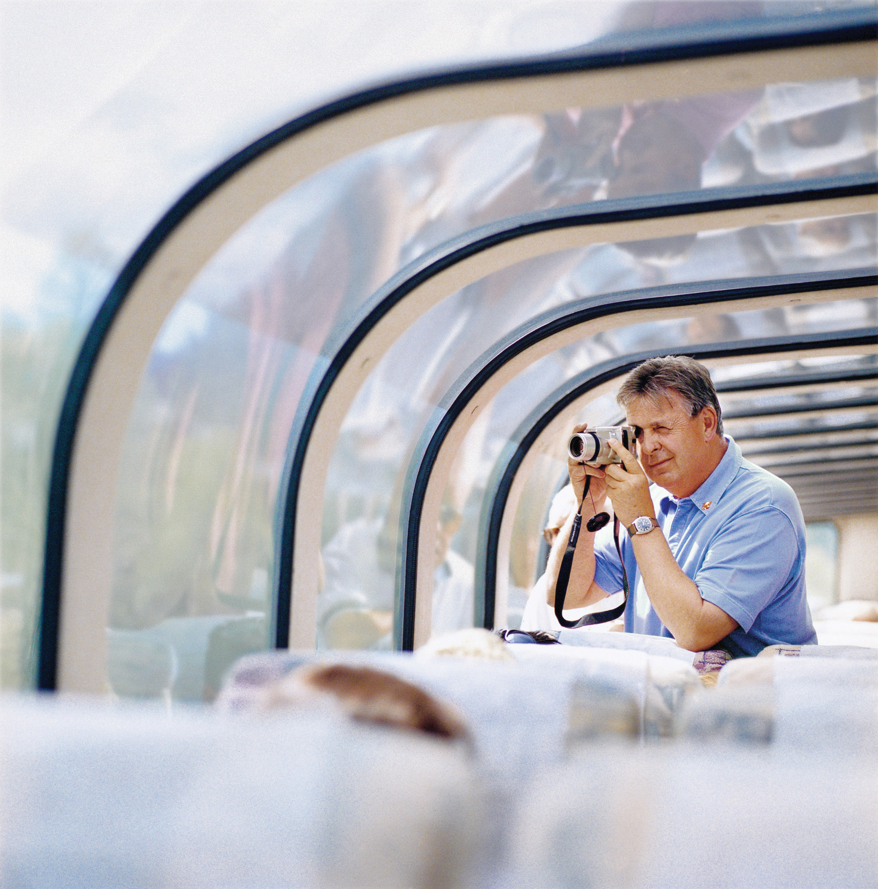 man taking a photo with a camera from the inside of the Rocky Mountaineer's iconic glass-dome coach in broad daylight