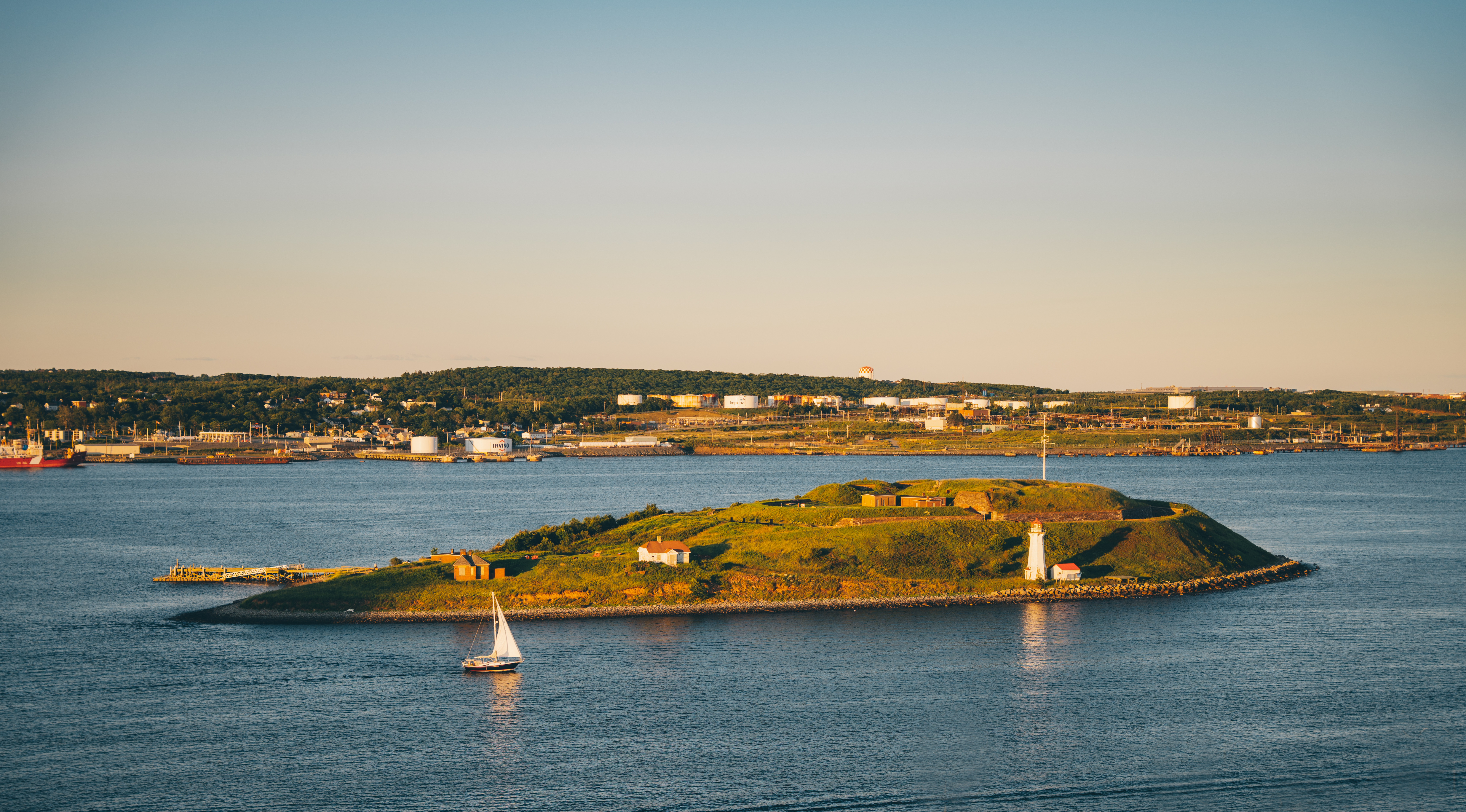 A sail boat cruises past a grassy island and harbour near Halifax