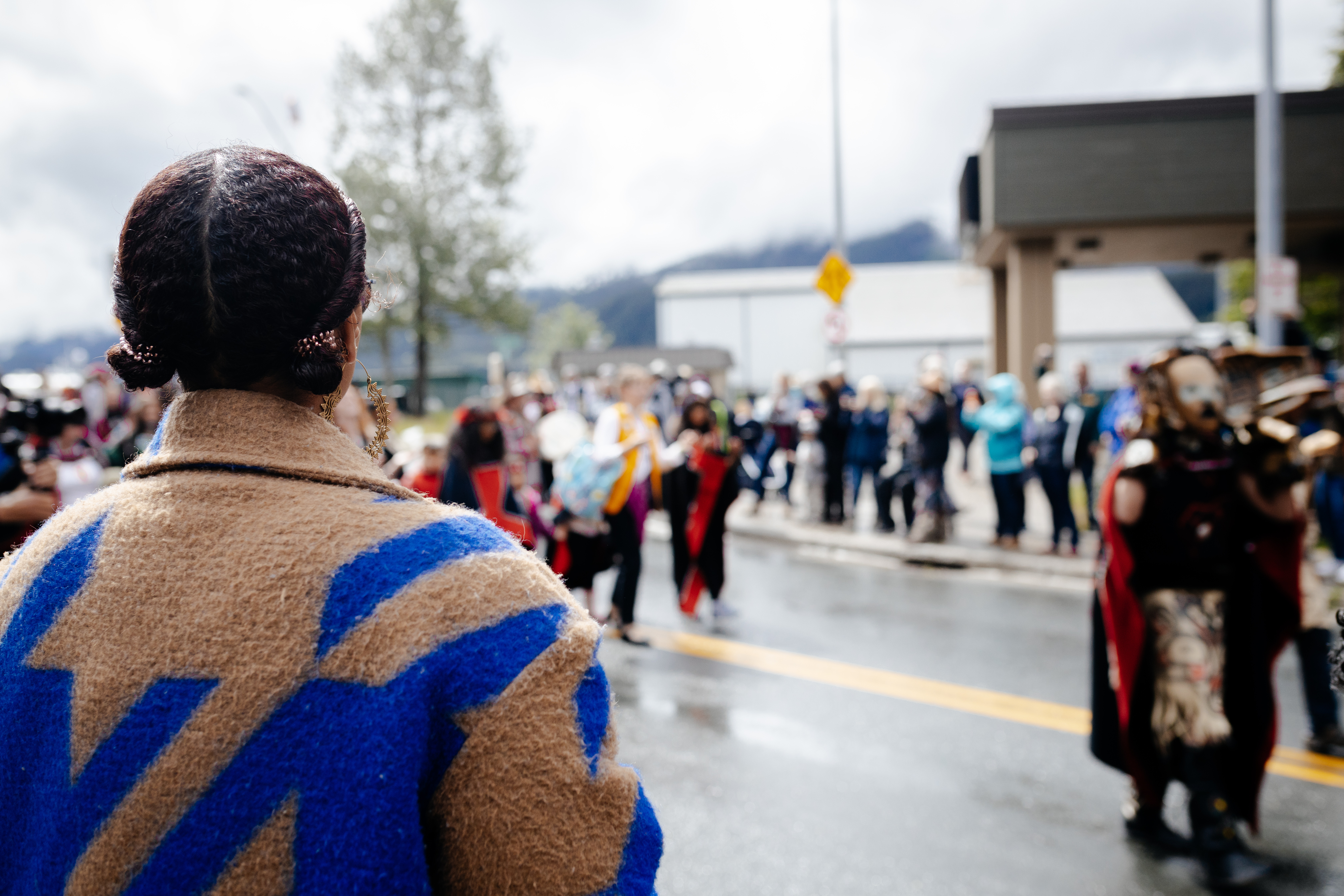 A person watches a street parade with people dressed in signature regalia of Southeast Alaska Nations