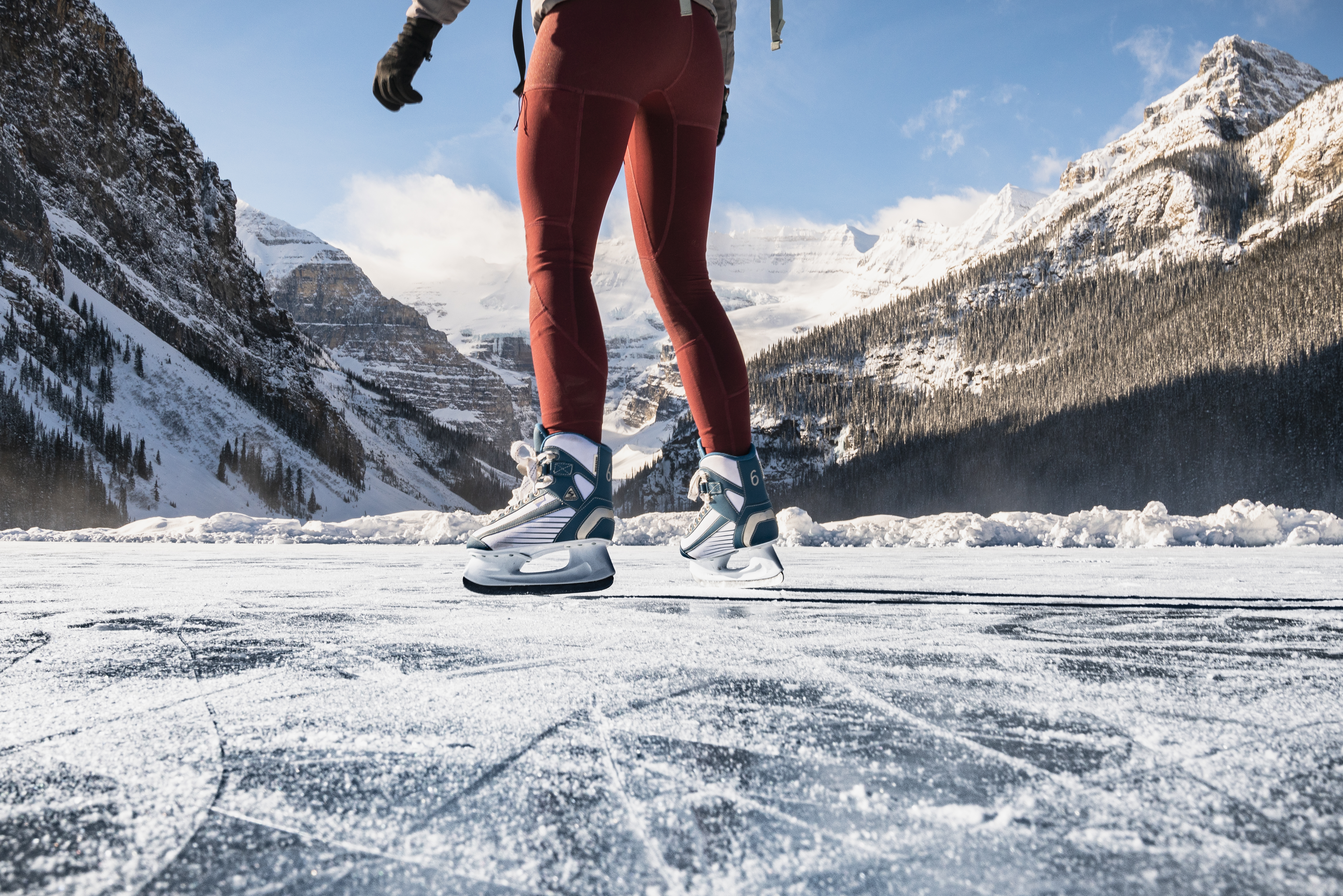 Close up of a person skating on frozen Lake Louise surrounded by snowy mountains