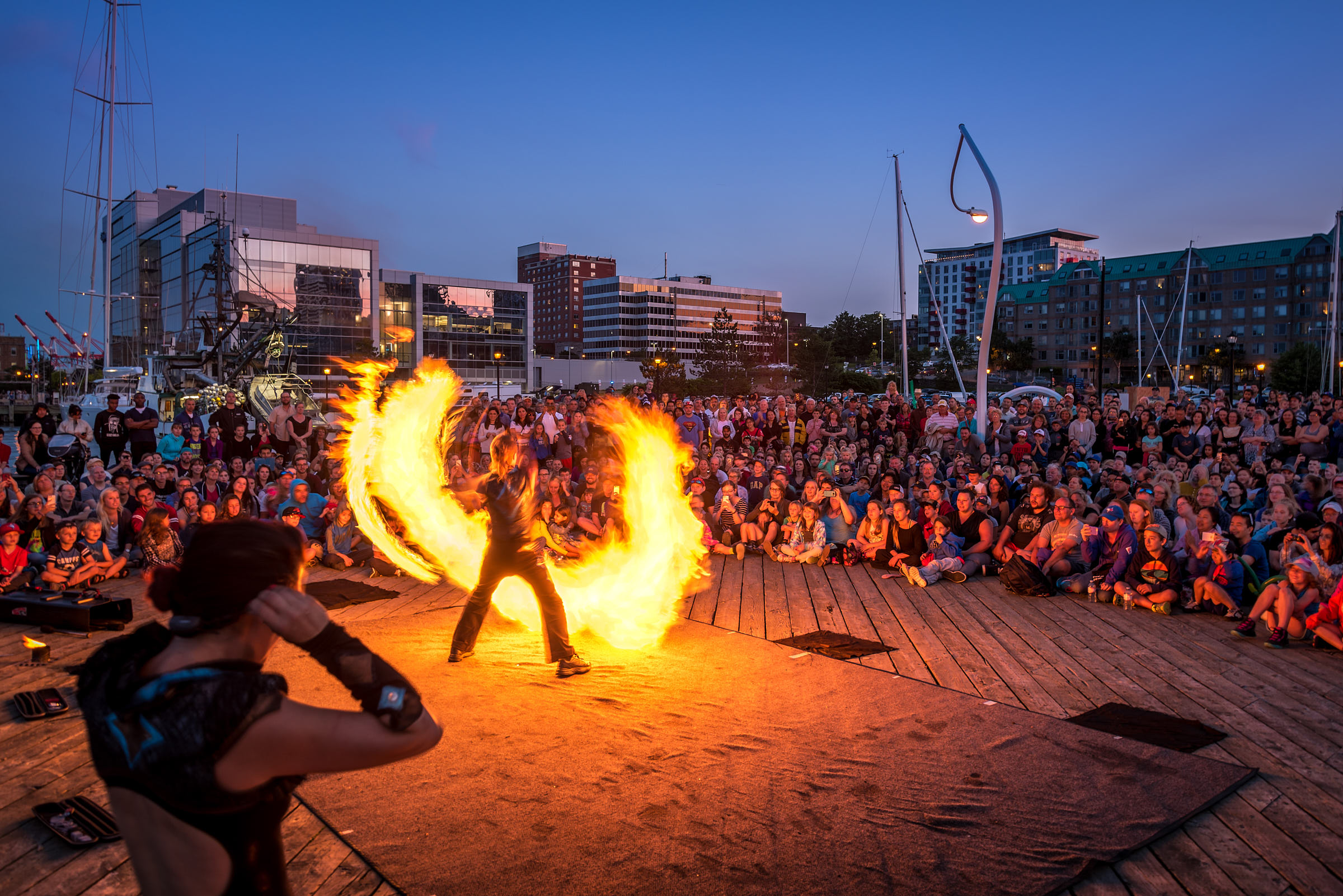 A large crowd sitting outside watching a flame throwing performer 