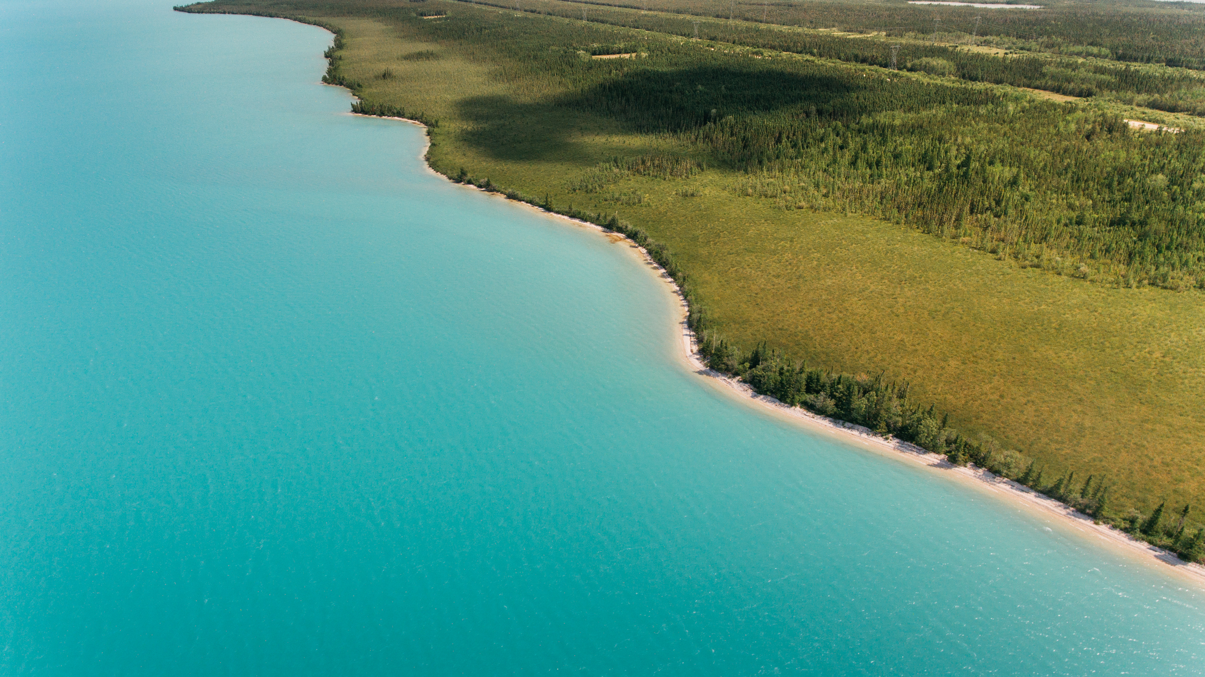 Aerial view of a large, bright turquoise lake in Manitoba