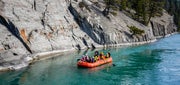 A red raft with a small group of people float down a green river in Jasper