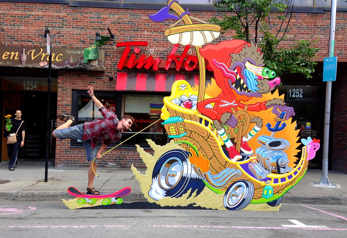 Man holds a string and poses next to a street art cartoon painting on a street in Montreal
