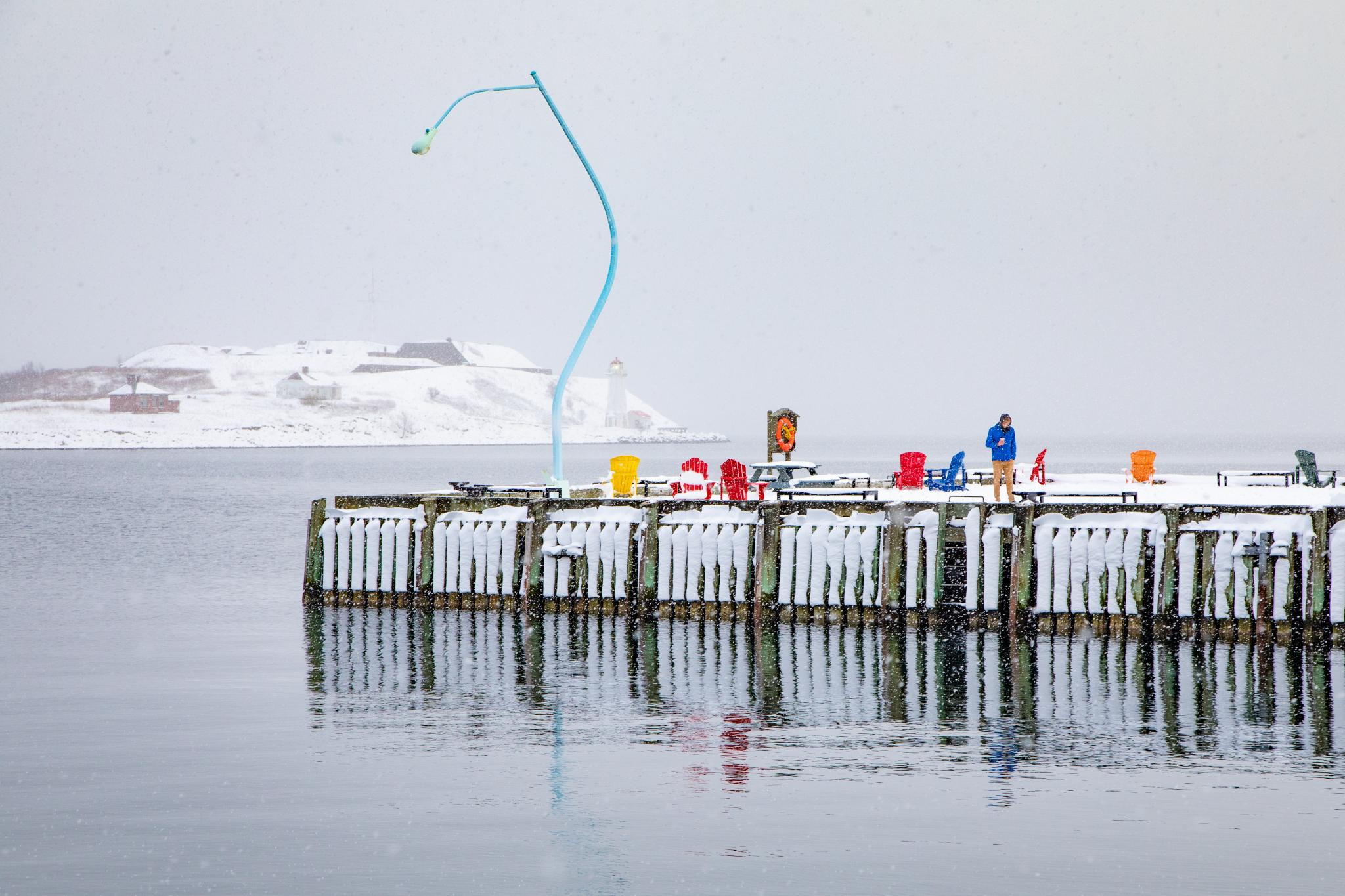 A boardwalk covered in snow, a bright blue lamppost and coloured chairs
