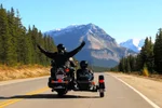 Two people driving through the Rockies on a motorcycle and sidecar