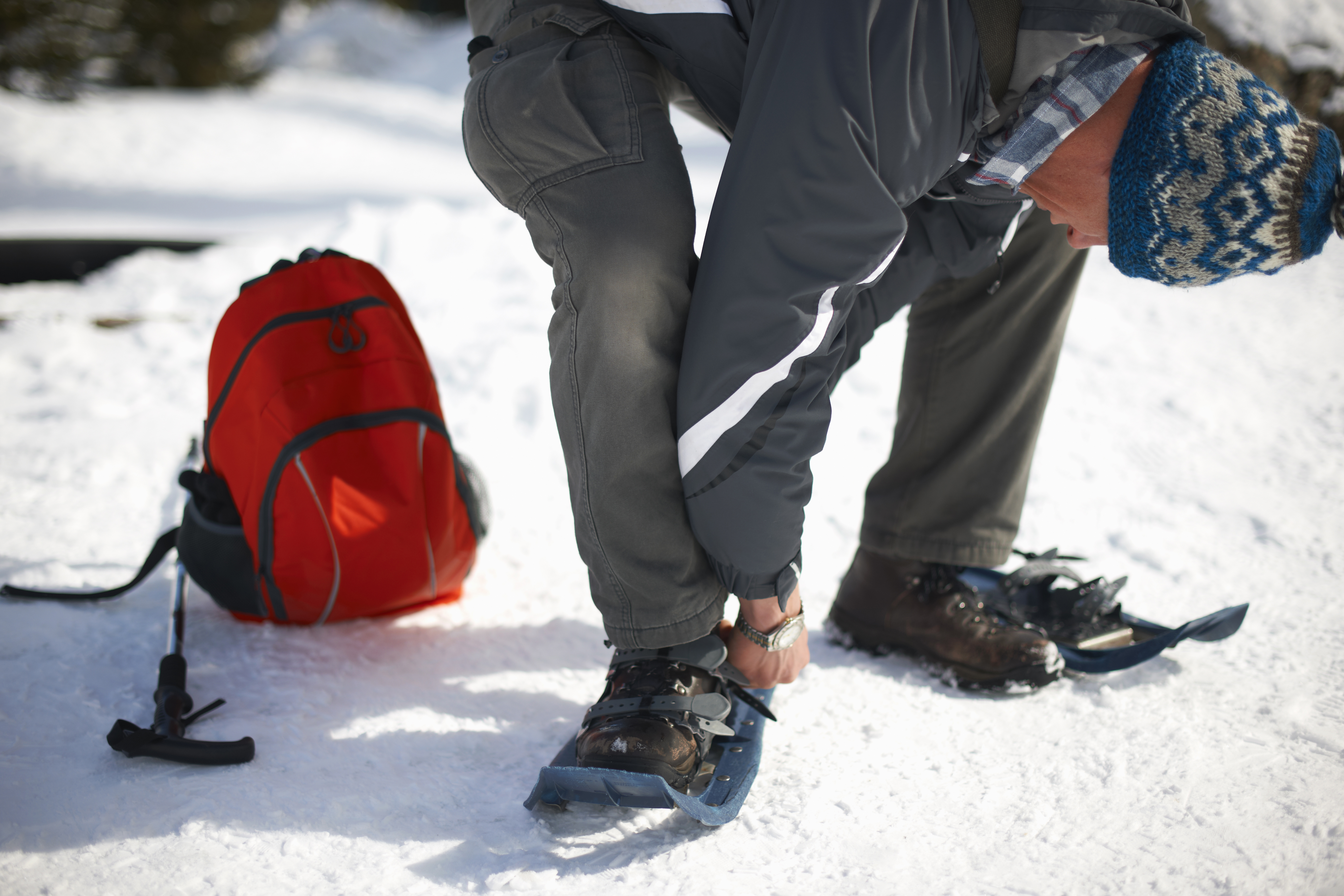 Man near backpack and pole stands and bends down enough to observe snowshoe on foot on a winter's day in Lake Louise, Canada