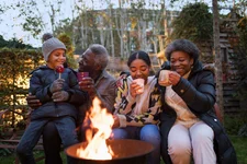 Grandparents and grandchildren drinking hot cocoa at campfire