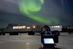 Camera on stand pointed to sky with visible northern lights in the sky near Tundra Buggy vehicle 