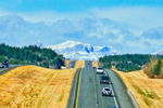 Cars on the highway with yellow grass along each side face snowcapped mountains