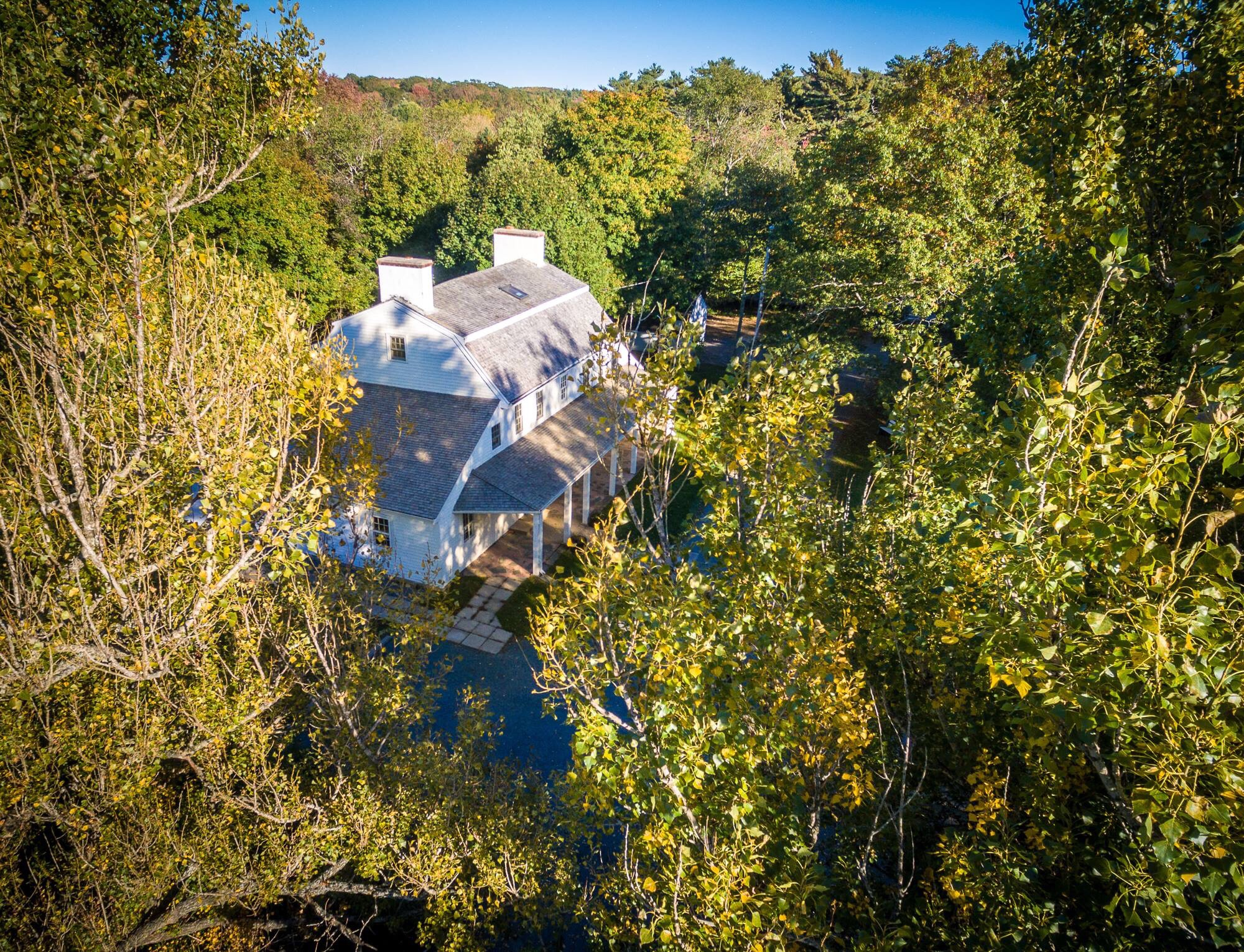 Aerial view of a two level manor house surrounded by trees in fall