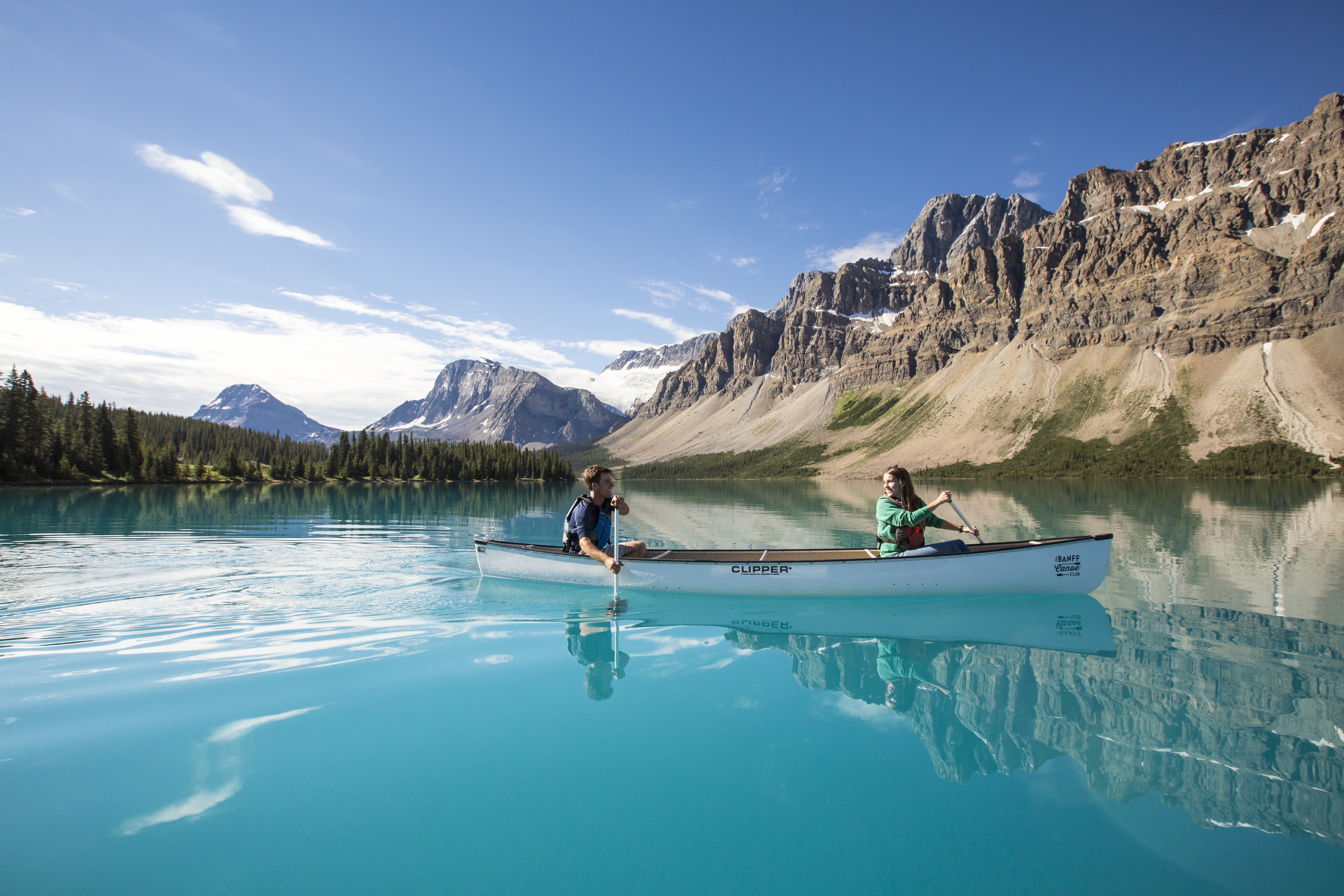 Two people paddling in a white canoe across bright blue lake in the Rockies