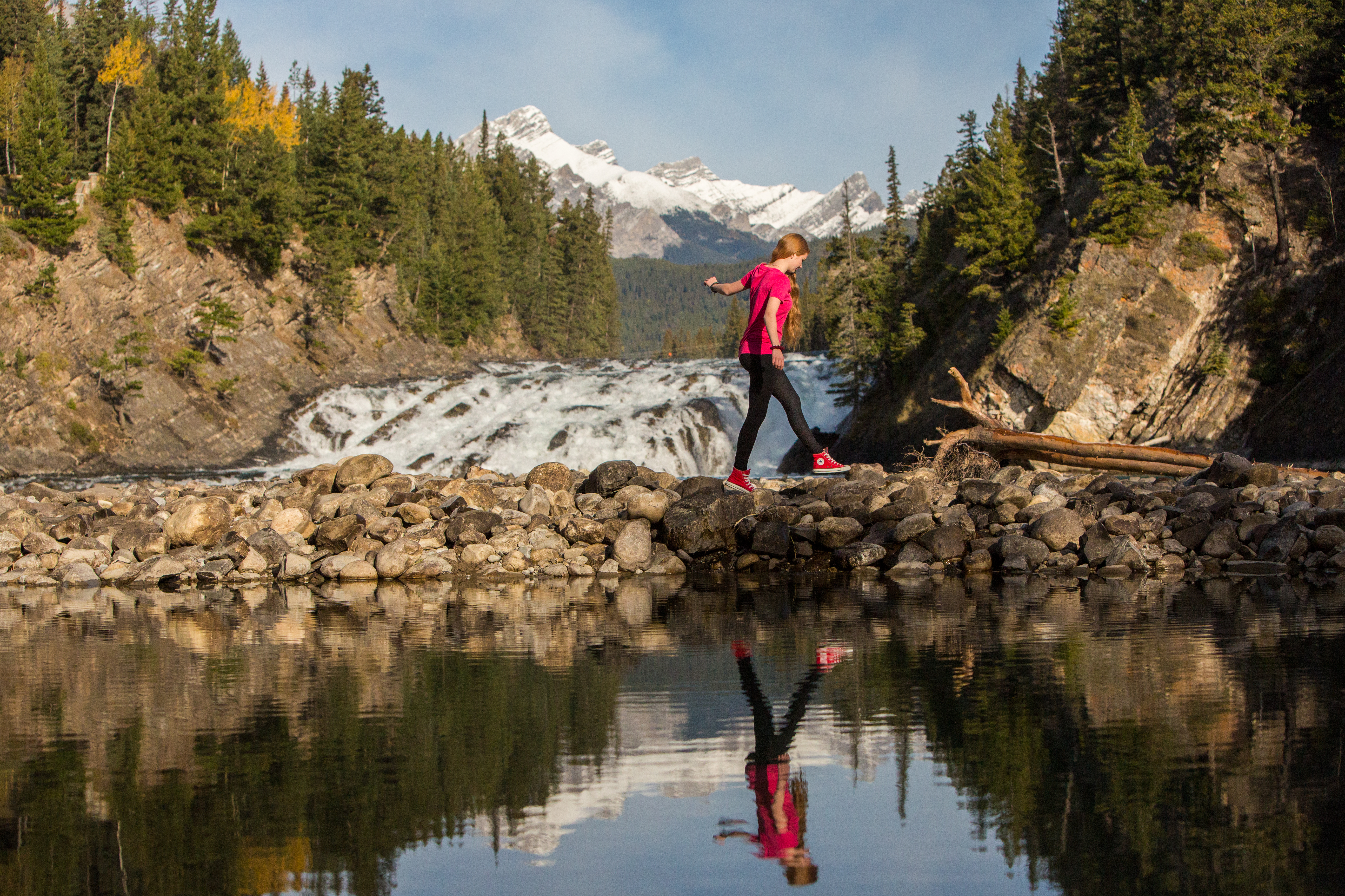 A person walking across rocks in front of Bow Falls beside the Bow River in Banff.