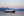 Small expedition ship cruises through Southeast Alaska at dusk with snowy mountains behind 