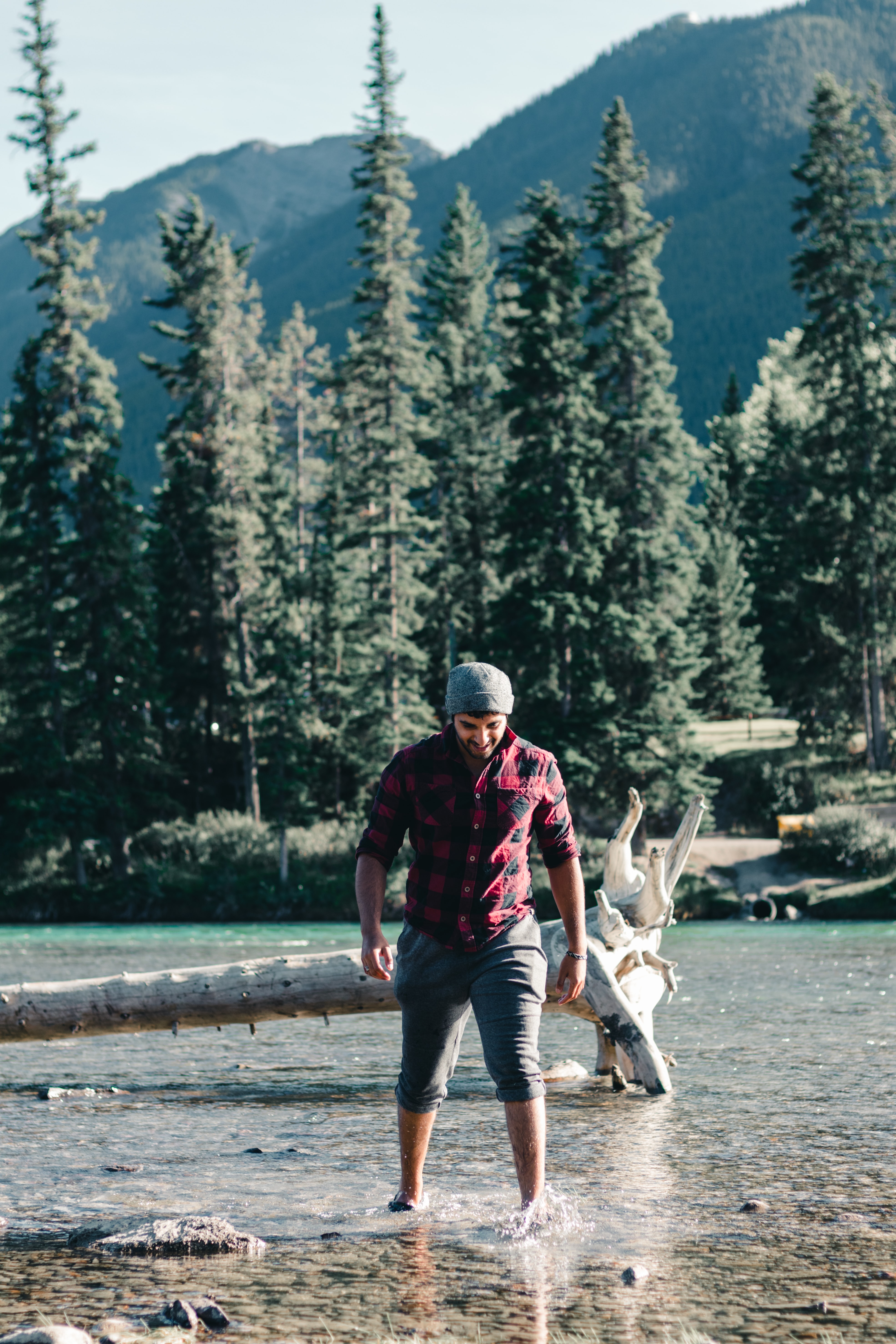 Man smiles and stands, while immersed in nature, in Tunnel Mountain Village campground with feet in shallow clean water