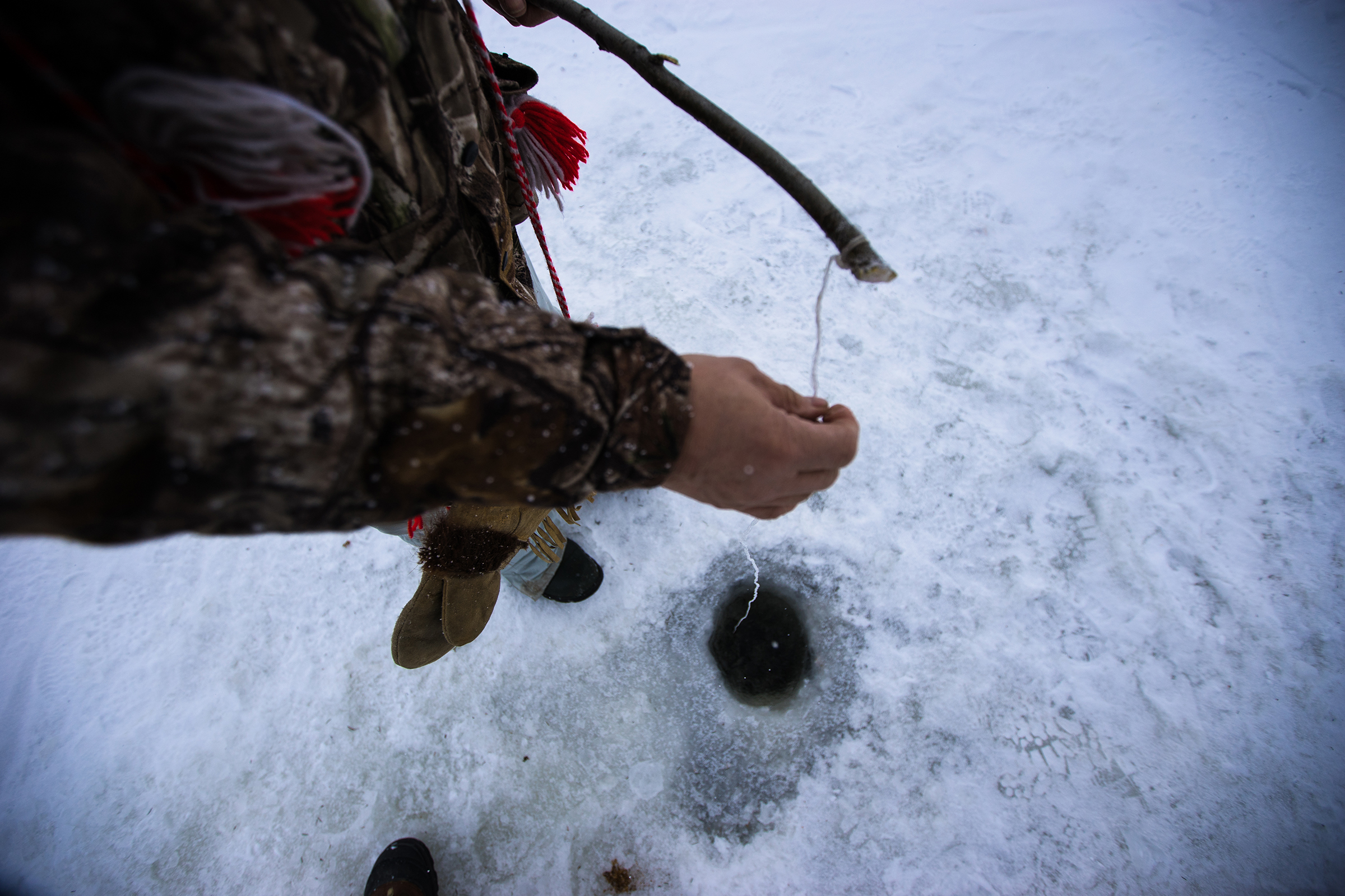  Ice fishing in Canada's Northwest Territories with rod made with wooden branch with line dipped into drilled hole and water under frozen lake