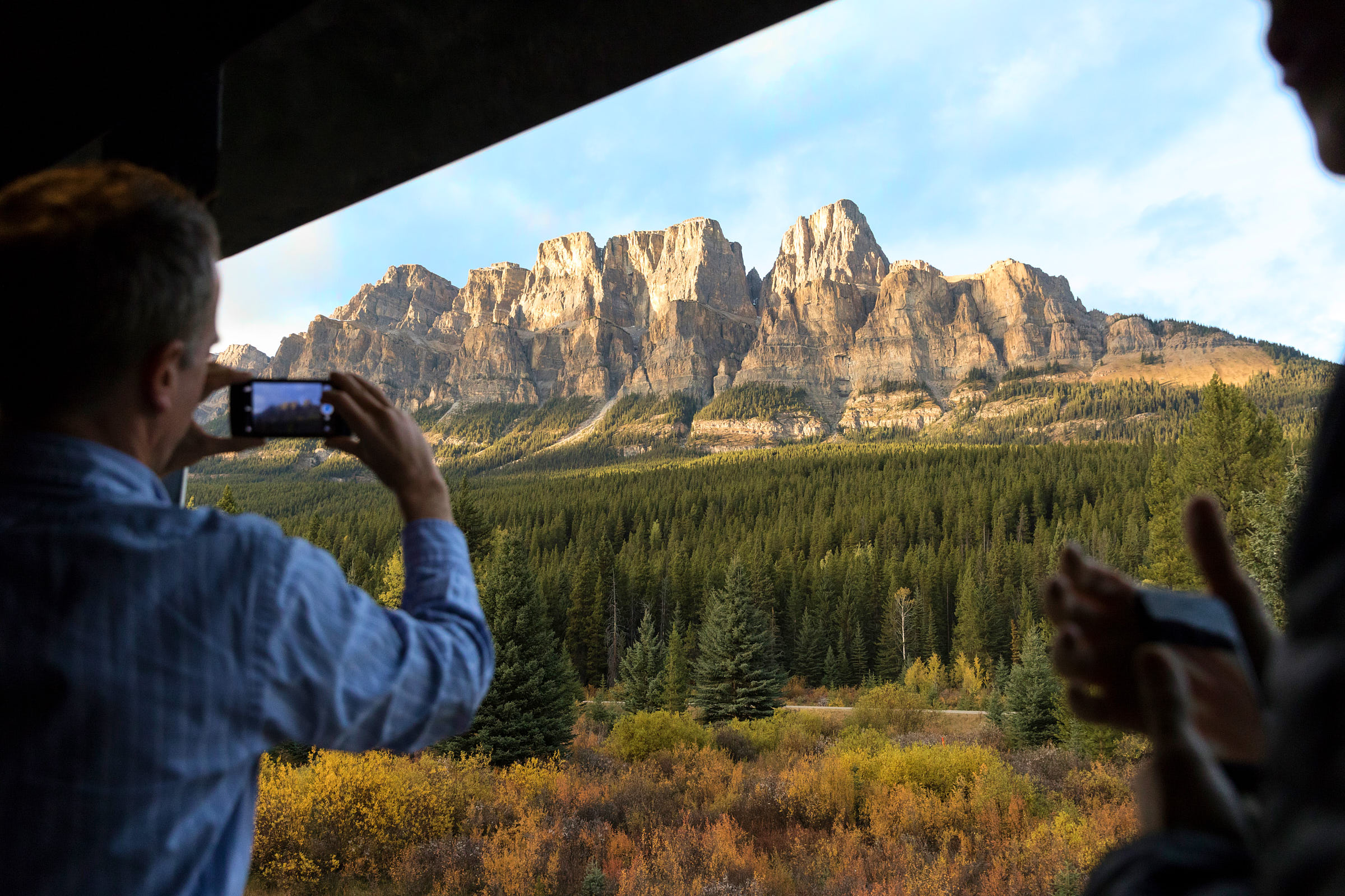 A guest taking a photo of the scenery from the GoldLeaf outdoor viewing platform of the Rocky Mountaineer train