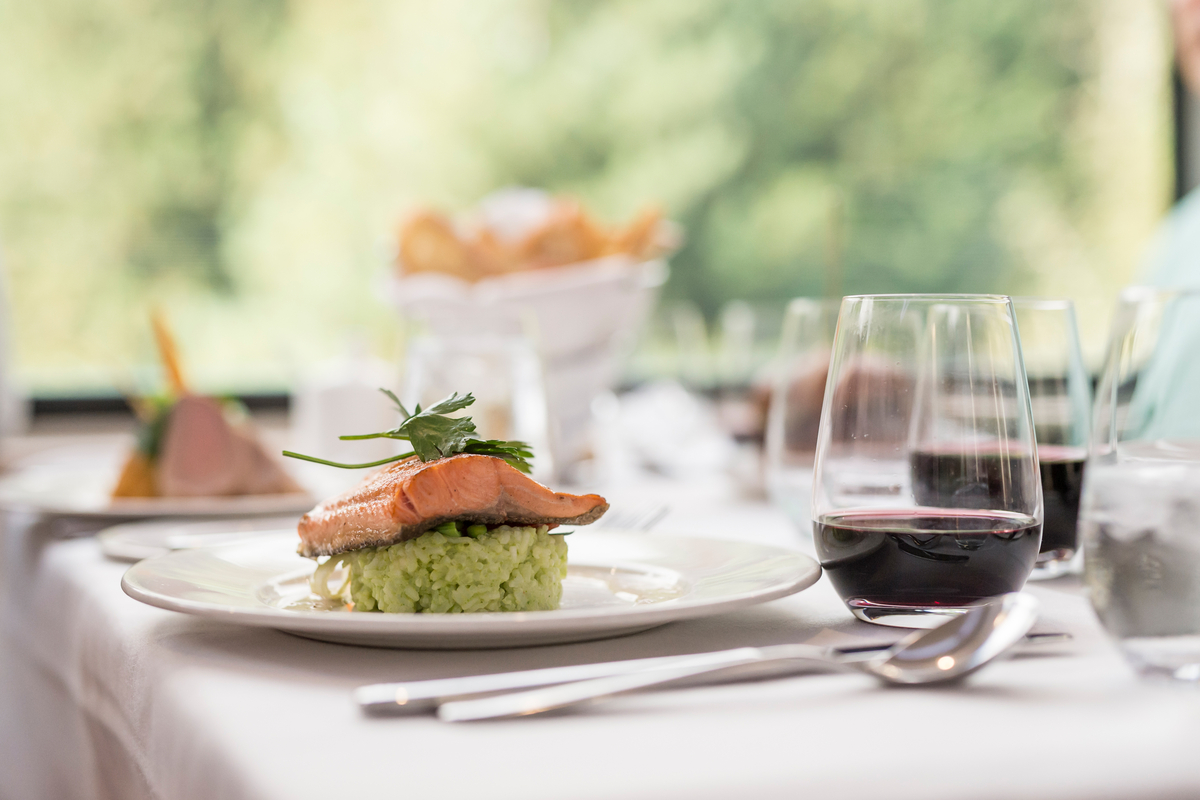 Salmon main dish and glass of red wine on an elegant table in the Rocky Mountaineer GoldLeaf service dining room