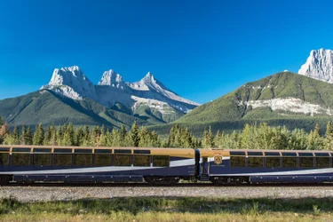 Two train coaches of the Rocky Mountaineer train with mountains and blue sky in the background