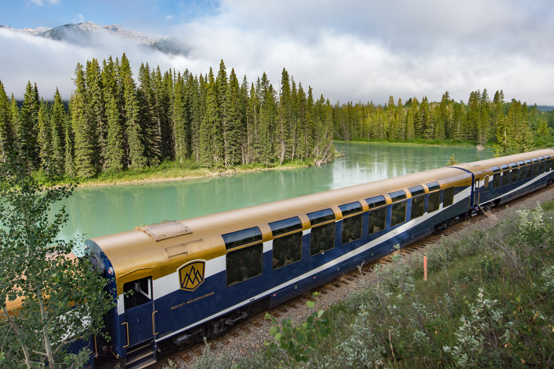The Rocky Mountaineer train rolling by a green river in the mountains.