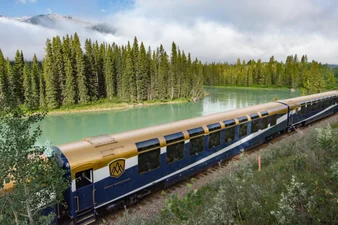 The Rocky Mountaineer train rolling by a green river in the mountains.