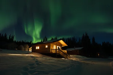 Green Northern Lights above a wooden cabin at Southern Lakes Resort in winter, snow on the ground