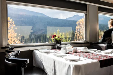 VIA Rail dining car offering view of mountains nearby with area complete with table set and seating for mealtime
