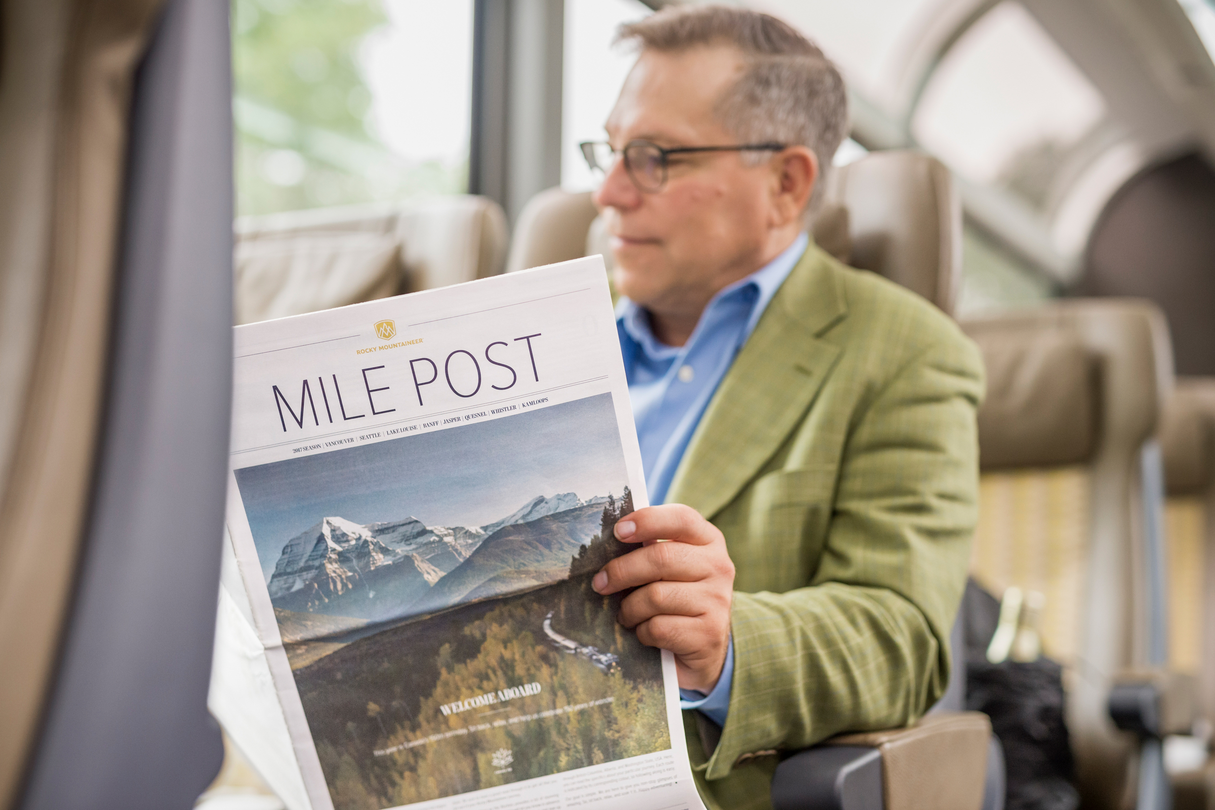 Man reading Mile Post newspaper onboard Rocky Mountaineer in SilverLeaf service