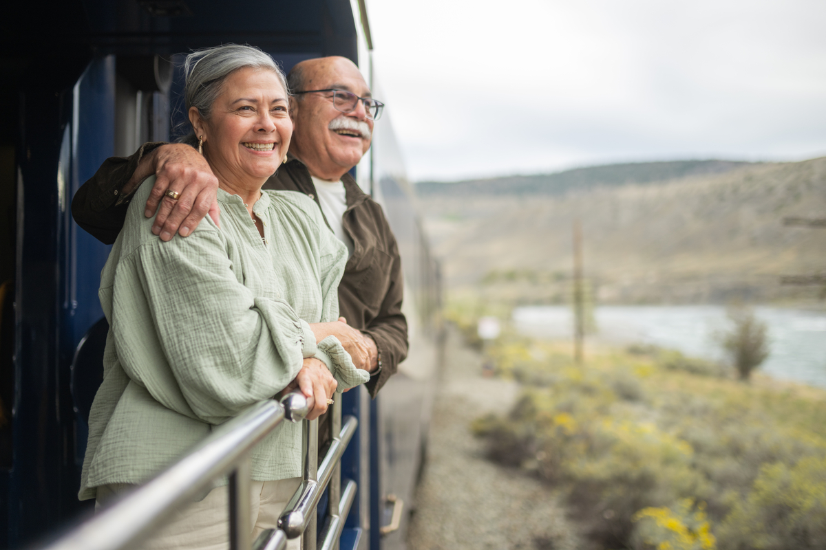 Guests looking at scenery from the outdoor viewing platform on the Rocky Mountaineer Train, mountain in the background