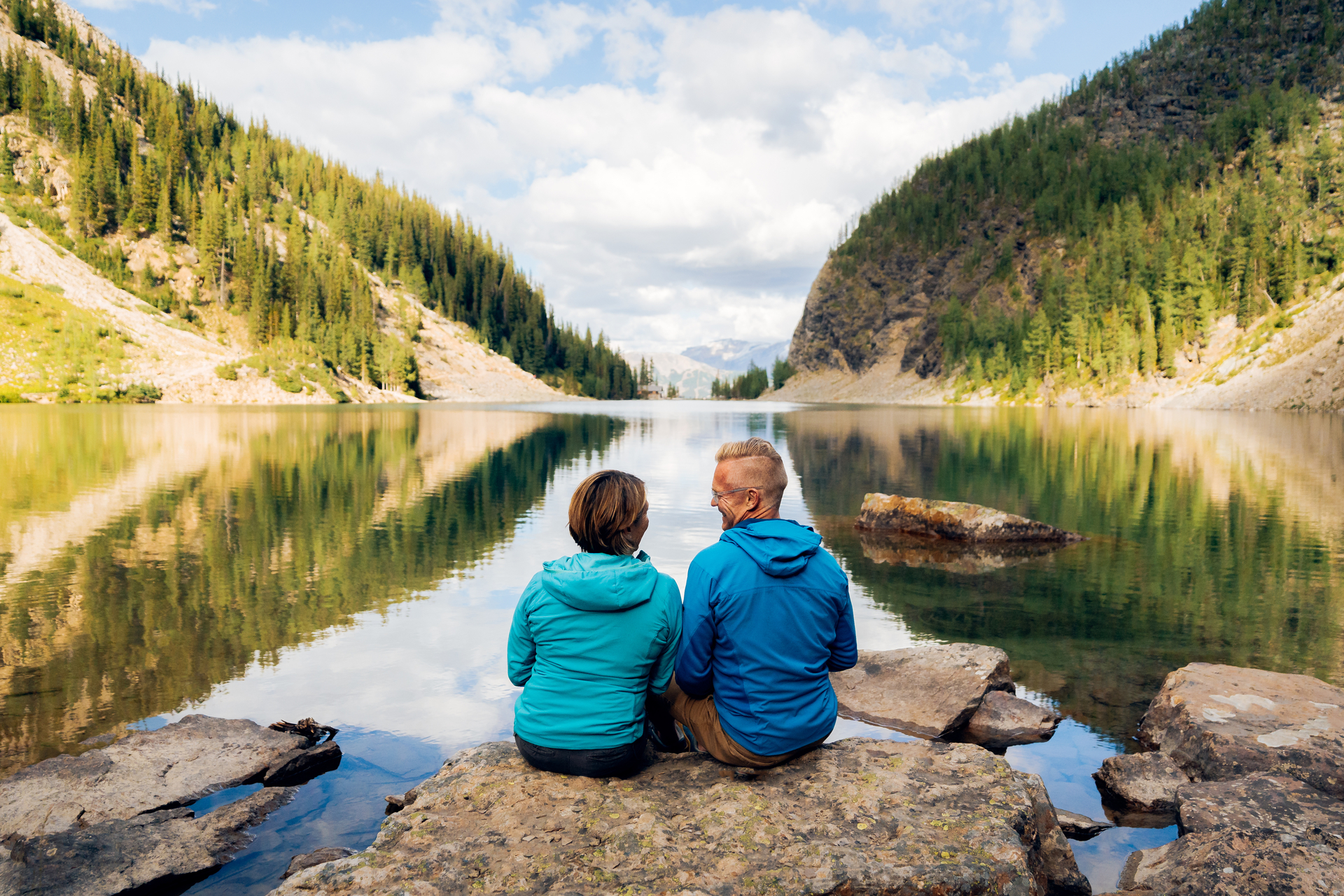 A couple sitting on a rock on the shore of Lake Agnes with mountains rising up on both sides