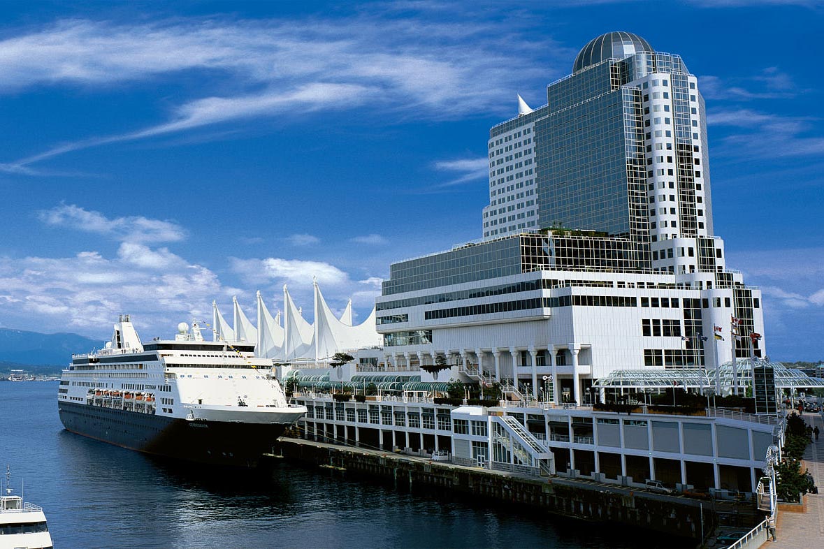 Pan Pacific Hotel towers over Vancouver harbour. A cruise ship is docked nearby.
