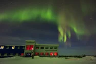 Auroral curtains in the north over the Churchill Northern Studies Centre, Canada, with a lone photographer setting up
