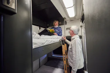Couple getting ready to sleep in bunk beds in a VIA Rail Sleeper Plus Cabin for two on The Canadian train