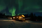 Green Northern Lights above a wooden cabin at Southern Lakes Resort in winter, snow on the ground