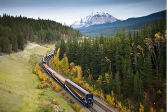 The Rocky Mountaineer train rounds a bend in the track near Mount Fitzwilliam, surrounded by fall colours trees.