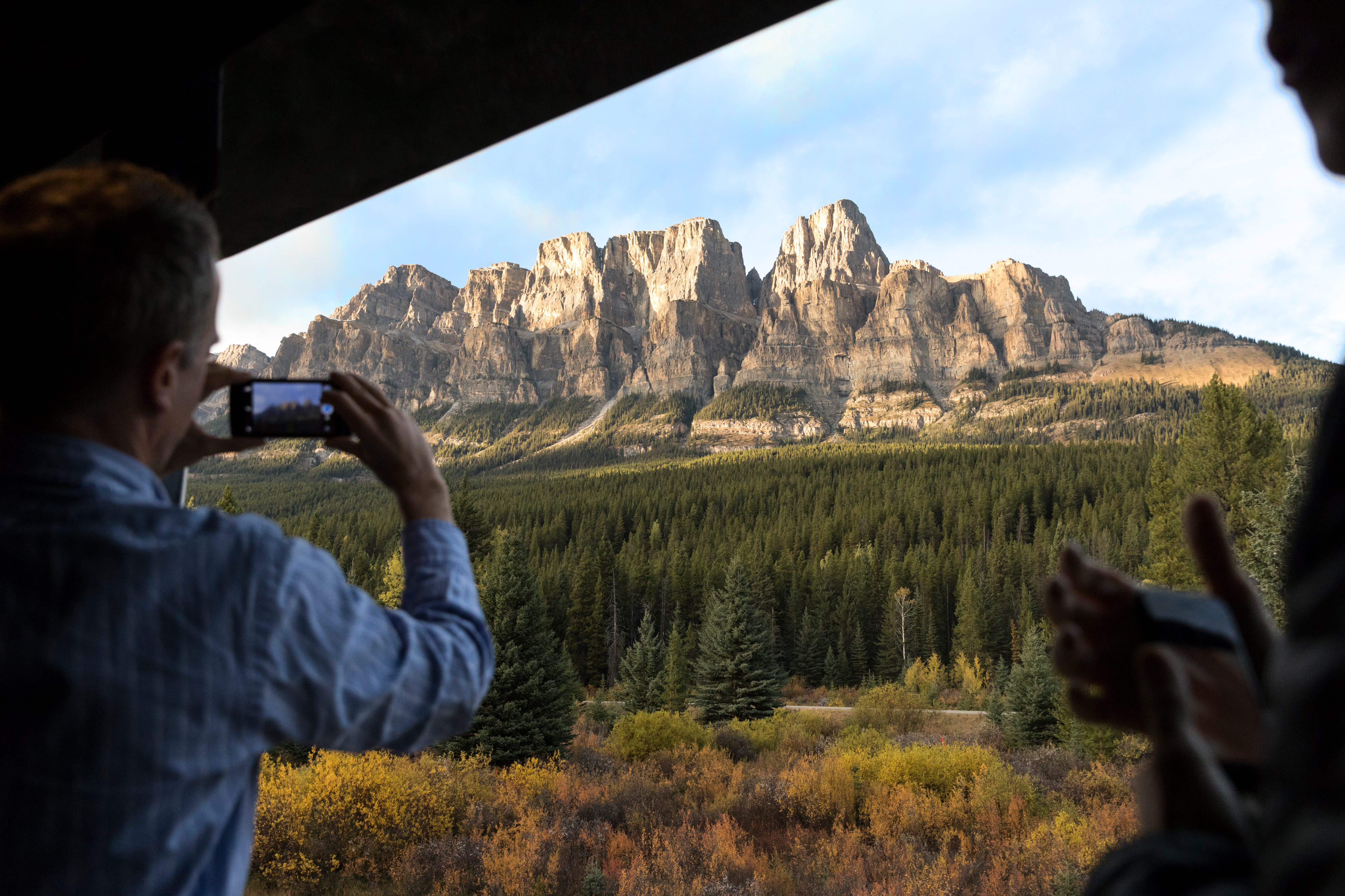 A guest taking a photo of the scenery from the GoldLeaf outdoor viewing platform of the Rocky Mountaineer train
