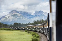 Rocky Mountaineer train rounding a bend in the track with a mountain range in the background.