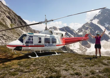 A woman poses next to a helicopter sitting at the top of a mountain